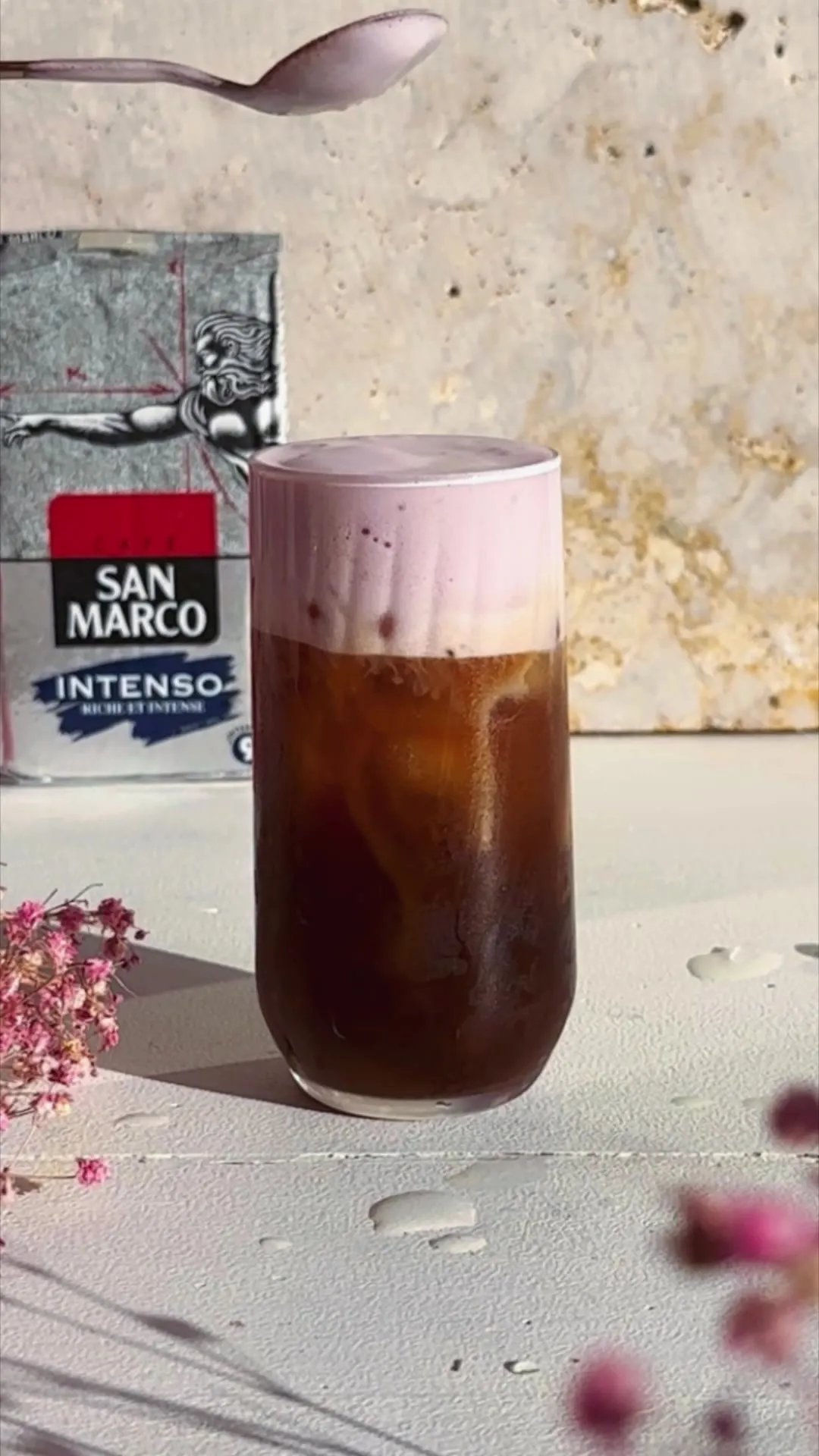 Café glacé surmonté d'une mousse rose, dans un grand verre