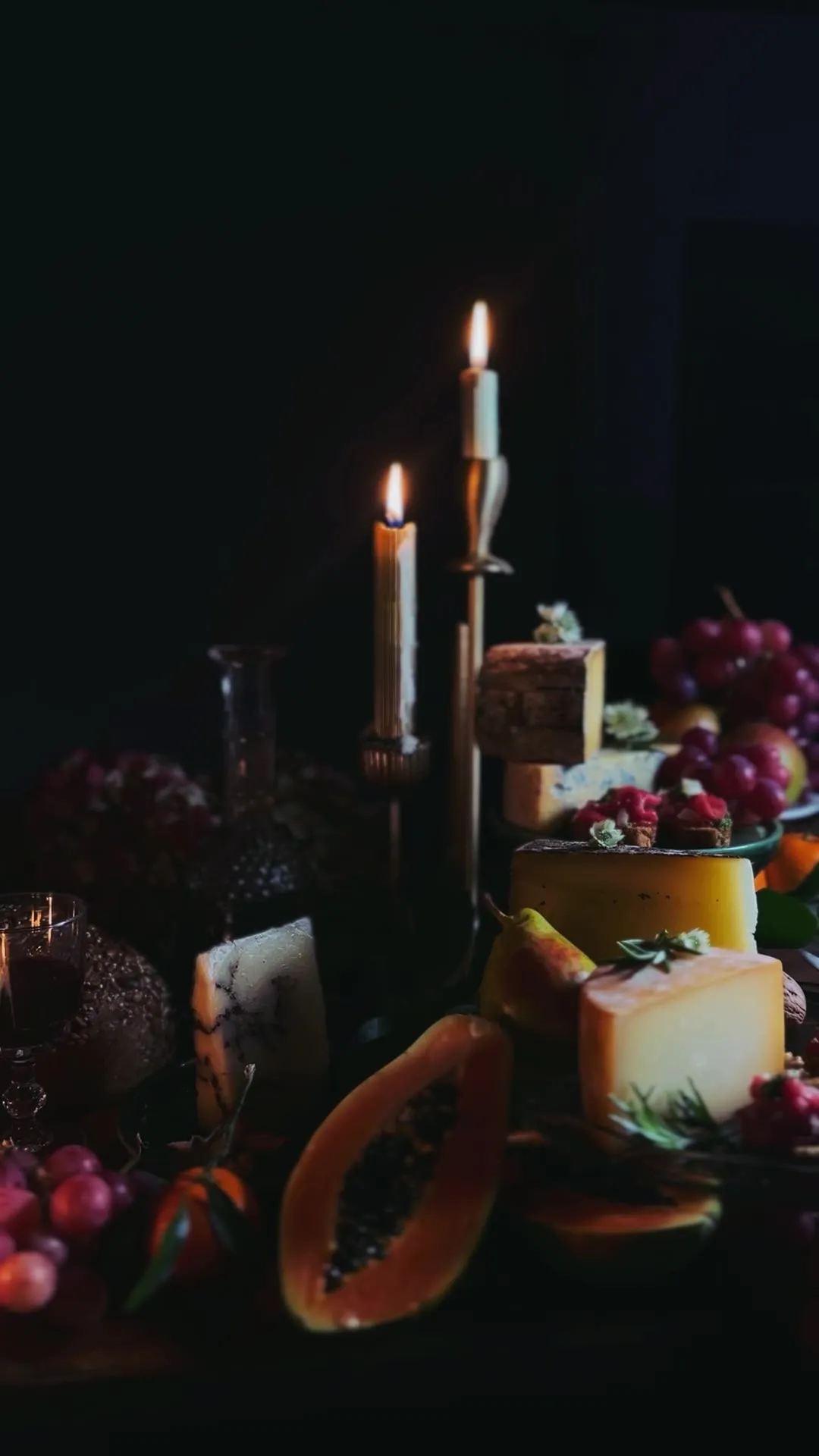 Nature morte de fêtes aux chandelles : fromages, fruits et raisins sur fond sombre
