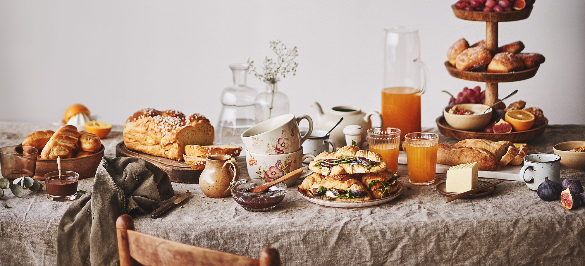 Table de petit-déjeuner dressée par Alexandra Pasti — viennoiseries, brioche, figues et jus d'orange sous un nuage de gypsophile